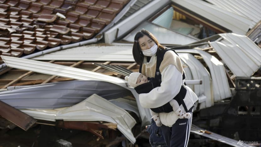 Một người phụ nữ bế con đứng trước ngôi nhà đổ sập do động đất ở Suzu, Ishikawa - Nhật Bản hôm 4-1. Ảnh: AP
