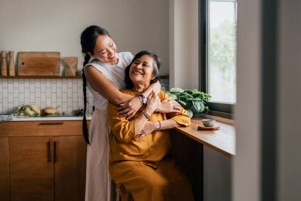 a-happy-beautiful-woman-hugging-her-mother-while-she-is-sitting-in-the-kitchen-and-drinking-17220139541932122752944.jpg