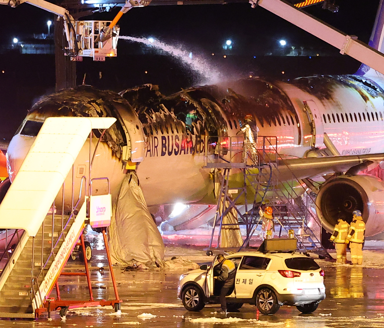 Firefighters check over the damaged Air Busan airplane following a fire at Gimhae International Airport in Busan, Wednesday. (Yonhap)