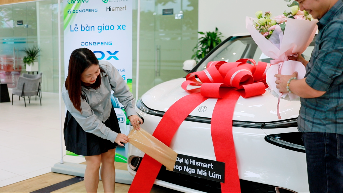 Hismart trao tặng xe điện Dongfeng Box cho đại lý: Kết nối thương hiệu, gắn bó cộng đồng - Ảnh 3. A person wrapping a gift on a car AI-generated content may be incorrect.