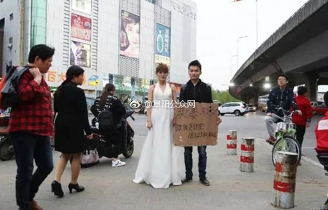 Trung Quốc: Người phụ nữ trẻ mặc váy cô dâu đứng giữa đường, chồng ở bên cạnh giơ biển bán vợ cứu con - Ảnh 1.