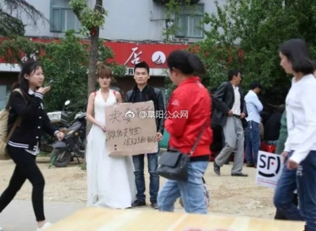Trung Quốc: Người phụ nữ trẻ mặc váy cô dâu đứng giữa đường, chồng ở bên cạnh giơ biển bán vợ cứu con - Ảnh 2.