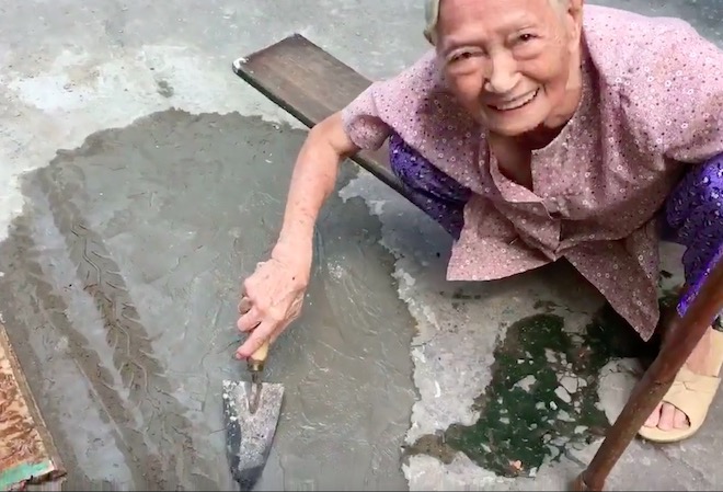 Xôn xao clip cụ bà ngoài 80 tuổi tự trộn xi-măng “vá” đường ở TP.HCM - Ảnh 1.