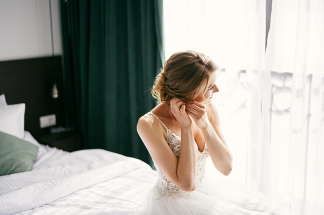 bride-sits-bed-by-window-putting-earrings-tilting-her-head-side278455-25293-1730271360806317013132.jpg