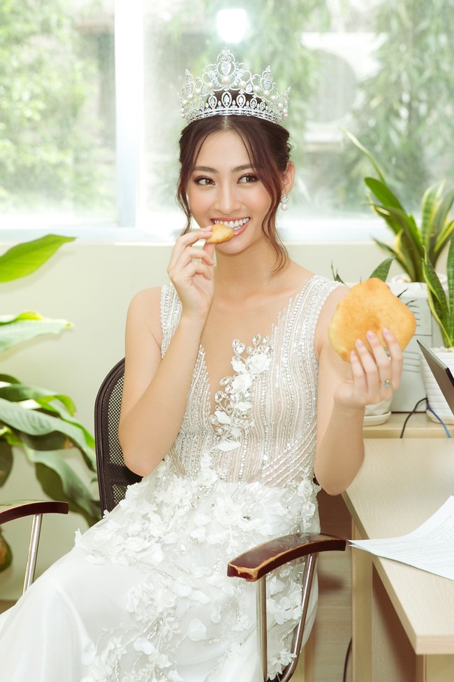 Hoa hậu Lương Thùy Linh đầu đội vương miện, tay bóc bánh ăn vội mà vẫn đáng yêu lạ thường  - Ảnh 1.